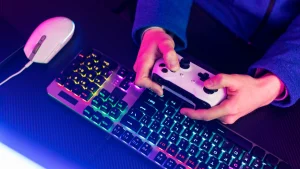 Person holding gaming controller above RGB mechanical keyboard and wired mouse Purpose: Clear and descriptive for accessibility tools and search engines.