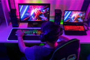 Gamer at dual-screen setup with RGB keyboard and neon-lit game visuals