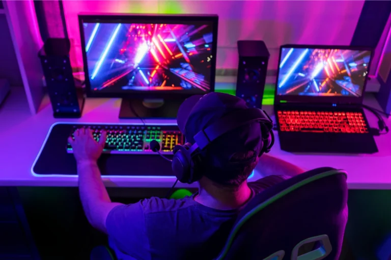 Gamer at dual-screen setup with RGB keyboard and neon-lit game visuals
