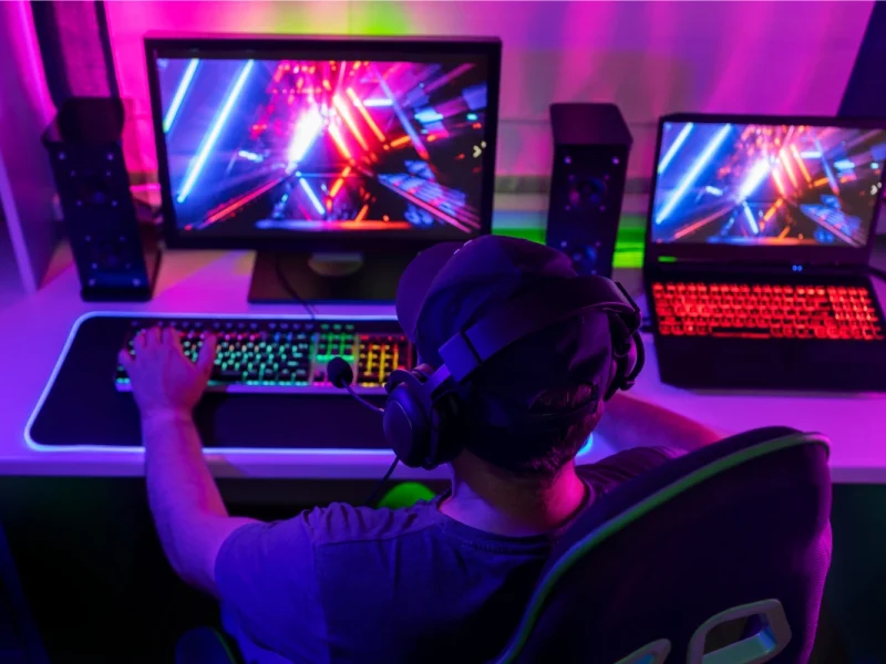 Gamer at dual-screen setup with RGB keyboard and neon-lit game visuals